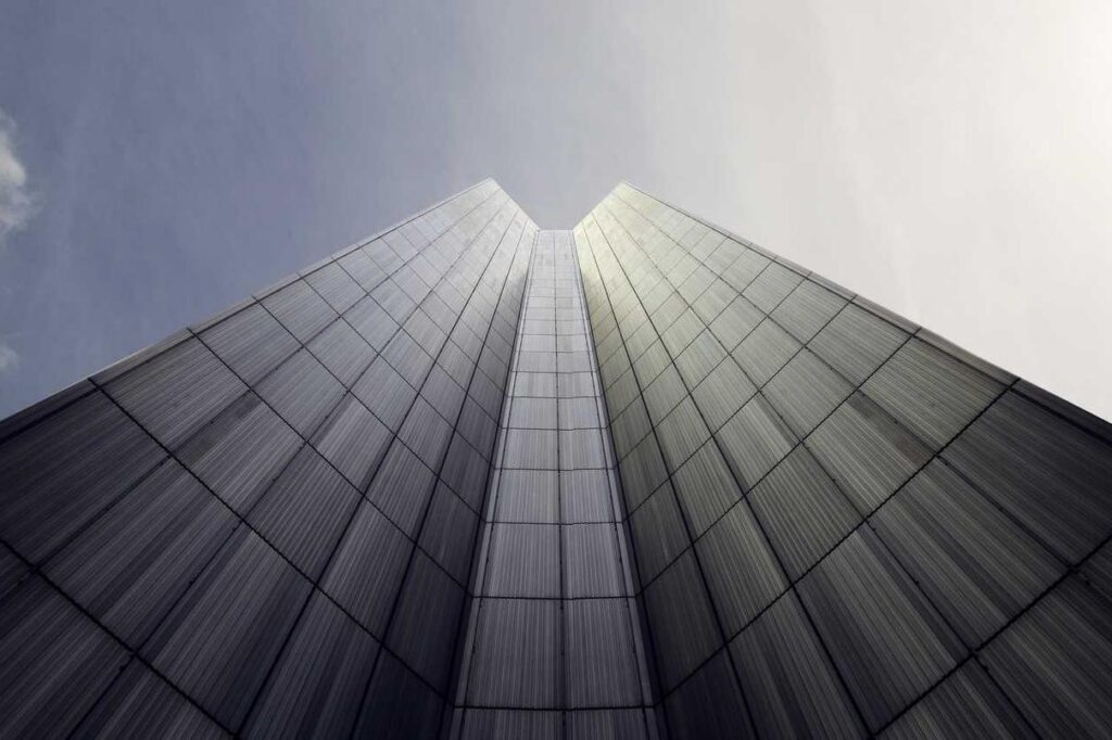 Low-angle view of a tall, modern glass building with symmetrical lines converging toward the sky, reflecting the interconnected nature of threat intelligence and cybersecurity under partly cloudy conditions.