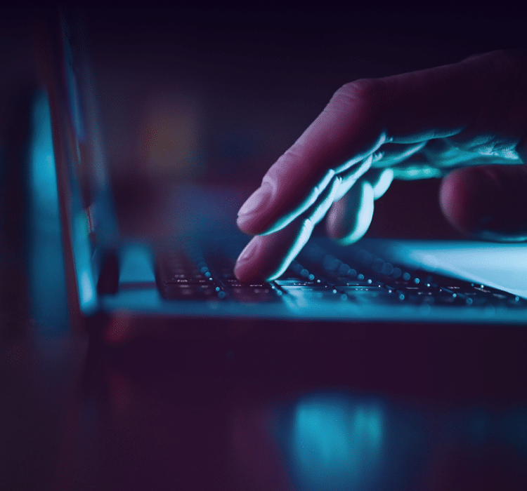 A close-up of a hand typing on a laptop keyboard in low light, with a blue and purple glow illuminating the scene—capturing the urgency of incident response in enterprise security and the world of cybersecurity.