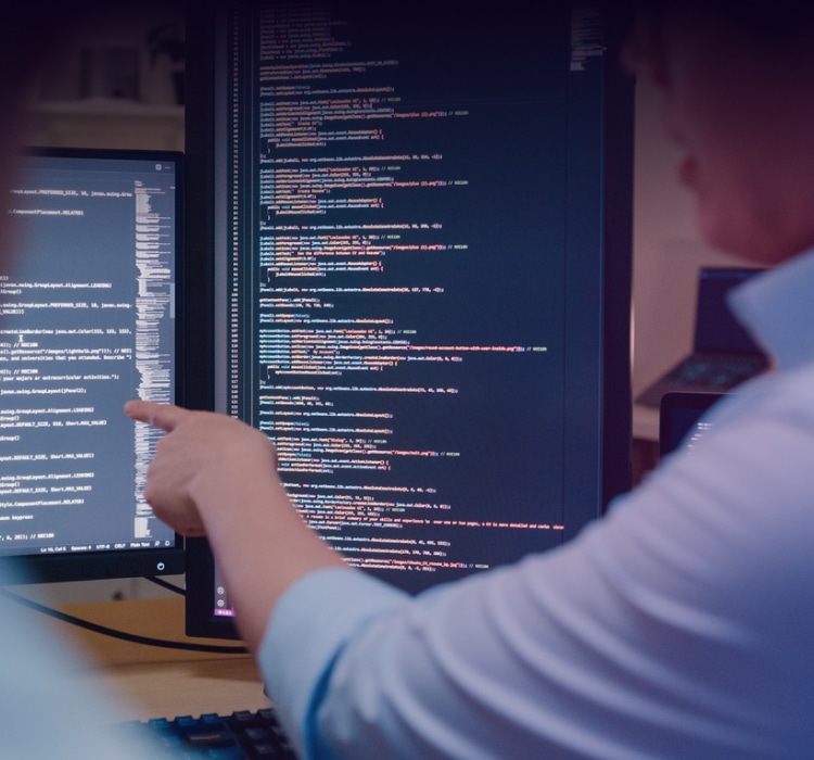 Two people are discussing code related to threat intelligence displayed on dual computer monitors; one person is pointing at the screen.